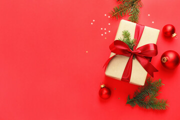 Fir tree branches, gift and Christmas decor on red background, flat lay. Space for text
