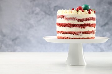 Delicious sponge cake with Christmas decor and red currants on white wooden table against grey background, closeup. Space for text