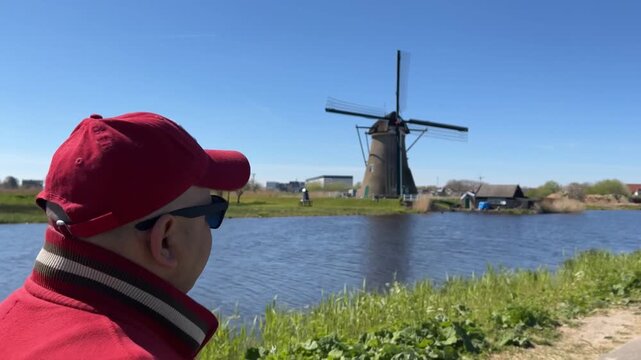 Hombre caminando observando molino al otro lado del canal