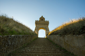 Historic stone steps ascending to a monumental archway under a bright blue sky at sunset
