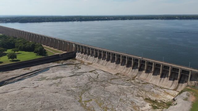 Wide aerial approach of Pensacola Dam with reservoir water stretching across northeastern Oklahoma landscape, cars cross on bridge