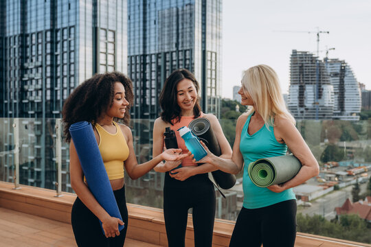 African American woman talks to mature blonde friend before yoga lesson on terrace 
