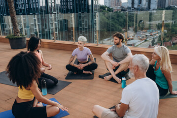Multigenerational people of different nations sit on rooftop terrace engaged in conversation at...