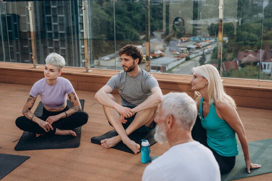 Group of different people sits in circle on rooftop engaged in conversation during break at yoga session outdoor - Powered by Adobe