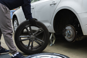 Young man changing the punctured tyre on his car loosening the nuts with a wheel spanner before jacking up the vehicle