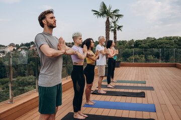 Focused multiethnic men and women enjoy yoga exercises on hotel rooftop