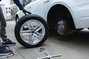 Young man changing the punctured tyre on his car loosening the nuts with a wheel spanner before jacking up the vehicle