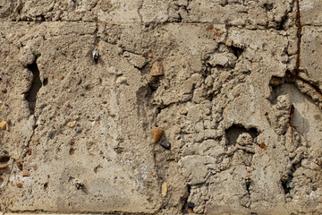 Texture of an aged concrete wall showing cracks and stones in an outdoor setting illuminated by natural light during the day