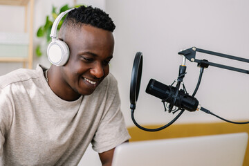 Teenage African student recording podcast with laptop and microphone at home. Young content creator sharing thoughts and stories online while developing communication and digital media skills