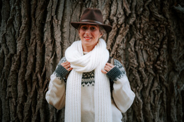 Happy traveler woman with backpack and hat standing in front of an old tree surrounded by sunlight...