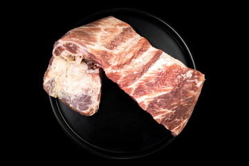 Freshly cut pork belly displayed on a round black plate, showcasing its marbled texture, perfect for grilling or roasting in home kitchens