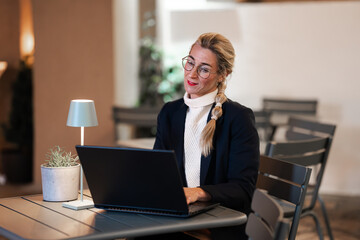 Attractive woman working on laptop in dim evening office showing modern business style and...