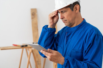 Worried construction worker checking tablet in a building