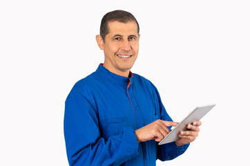 Confident smiling professional handyman in blue overalls using digital tablet with white background.