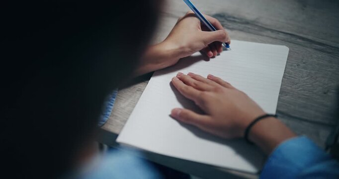 Businessman person is writing on a piece of paper with a blue pen. The person is sitting at a table and he is focused on their writing in slow motion. Scene is calm and focused.