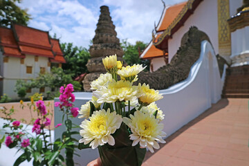 Closeup of flower bouquet for offering Lord Buddha with blurry Wat Phumin temple in the backdrop, Nan province, northern Thailand