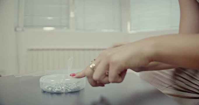 Close-up of a woman's hands creating satisfying ASMR sounds by manipulating small metal screws and fasteners in a clear plastic container.