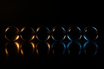Glass Spheres With Warm And Cool Light. A row of transparent glass spheres sits on a reflective black surface, softly glowing with orange and blue light to create a calm.