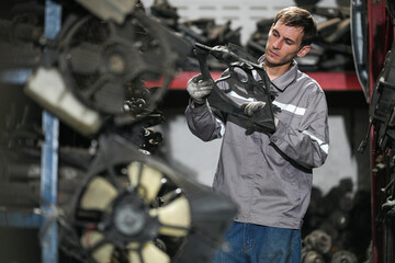 White man technician checking used car damaged engine block at scrap yard warehouse recycle area part. Maintenance engineer inspecting rust oily auto motor old spare part in junkyard for reuse service