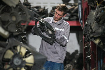 White man technician checking used car damaged engine block at scrap yard warehouse recycle area part. Maintenance engineer inspecting rust oily auto motor old spare part in junkyard for reuse service