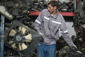 White man technician checking used car damaged engine block at scrap yard warehouse recycle area part. Maintenance engineer inspecting rust oily auto motor old spare part in junkyard for reuse service