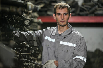 White man technician checking used car damaged engine block at scrap yard warehouse recycle area part. Maintenance engineer inspecting rust oily auto motor old spare part in junkyard for reuse service