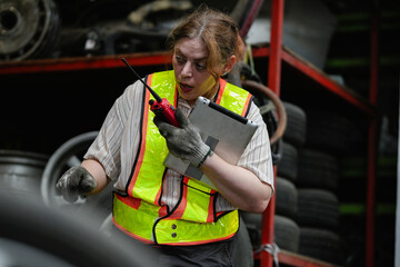 Fototapeta premium Female hispanic technician inspect used car damaged part at scrap yard warehouse recycle area. Latin maintenance engineer examining oily auto motor tires old spare part in junkyard for reuse service