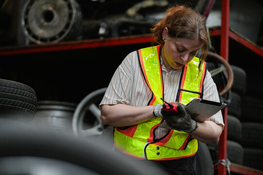 Female hispanic technician inspect used car damaged part at scrap yard warehouse recycle area. Latin maintenance engineer examining oily auto motor tires old spare part in junkyard for reuse service