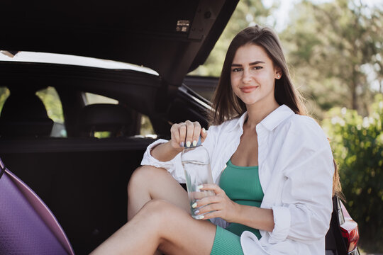Smiling woman in sportswear stands by the water, holding a phone, with a bridge in the background.