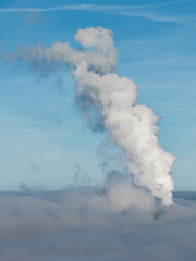 Aerial drone view of industrial chimneys emitting steam above thick fog and clouds on a sunny day, power plant and factory landscape. Panorama above clouds in fog in sunny day. Clouds factory