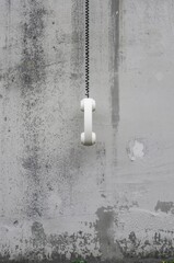 A striking and evocative image features a vintage white telephone receiver suspended by its coiled black cord against a heavily textured, distressed grey wall. The weathered concrete surface, with its