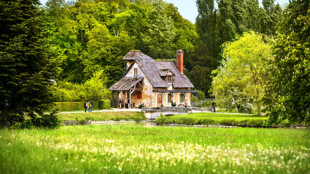 View of rustic charm exudes from the quaint cottage nestled amid lush greenery and a tranquil pond, a picturesque scene, Versailles, ÃŽle-de-France, France.