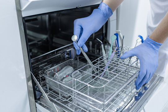 Sterilization of dental instruments in autoclave tray with gloved hands in clinic - Powered by Adobe