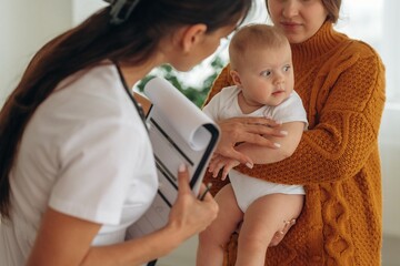 Notepad is in hands. Mother with her little baby daughter is in clinic with doctor at appointment