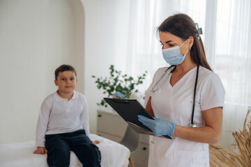 Obraz premium Writing notes into notepad. Boy is in routine appointment in clinic with female doctor