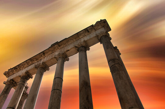 Fototapeta View of ancient stone columns reaching towards a fiery sunset sky, casting long shadows and evoking a sense of timeless grandeur, Rome, Italy.