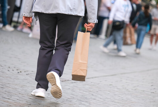 Menschen unterschiedlichen Alters beim Einkaufen mit in der Stadt &ndash; selektiver Fokus auf eine Frau im Vordergrund mit einer Einkaufst&uuml;te in der Hand, viel Copyspace