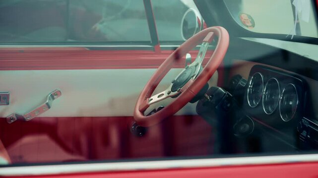 Close up of a vintage car interior shot through the window, focusing on the red steering wheel and dashboard