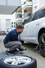 Young man unscrewing lug nuts on a car wheel with a wrench while replacing a flat tire on the road