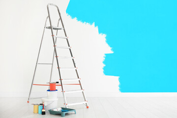 Decorator's tools and paint on floor in room. Wall partly painted in light blue color. Interior renovation
