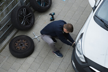 Man changes car tires outdoors using tools focused on vehicle maintenance and repair on pavement in urban area during seasonal tire replacement