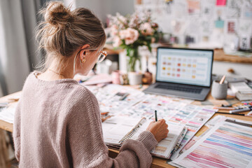 A creative workspace with a woman planning and designing, surrounded by color swatches, a laptop, and floral arrangements.