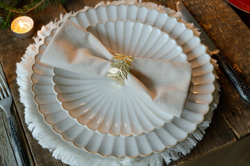 Elegant Christmas crockery, table decor. Table setting with white plates, linen napkin and decorative elements. 
