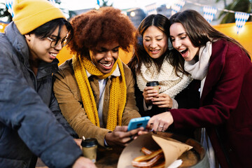 Four cheerful multi-ethnic friends looking at smartphone and having fun together at wintertime at a...