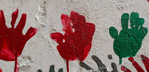 Red and green handprints painted on textured white wall image