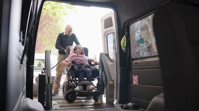 Caregiver assisting man with disability in wheelchair onto accessible van lift