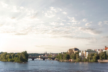 Obraz premium The Vltava river flowing through Prague on a summer day with boats and clouds