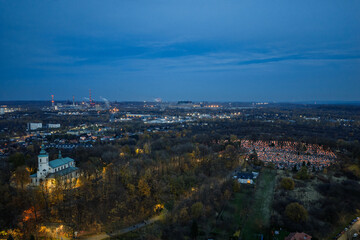 Cemetery on All Saints Day evening with glowing candles and lanterns illuminating graves, warm light reflecting on tombstones creating peaceful atmosphere of remembrance and tradition