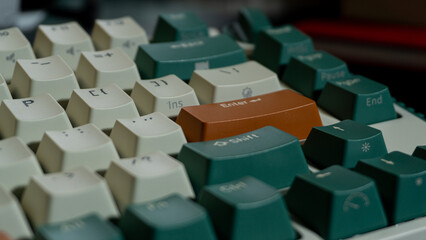 Macro photo of orange Enter key surrounded by green and beige keycaps, focus on key textures with blurred edges creating a balanced composition.