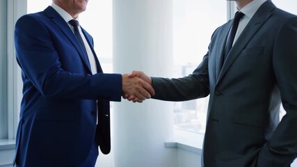 Successful business: Two businessmen (senior and young) shake hands in a modern office, symbolizing collaboration, agreement, and a professional partnership. - Powered by Adobe